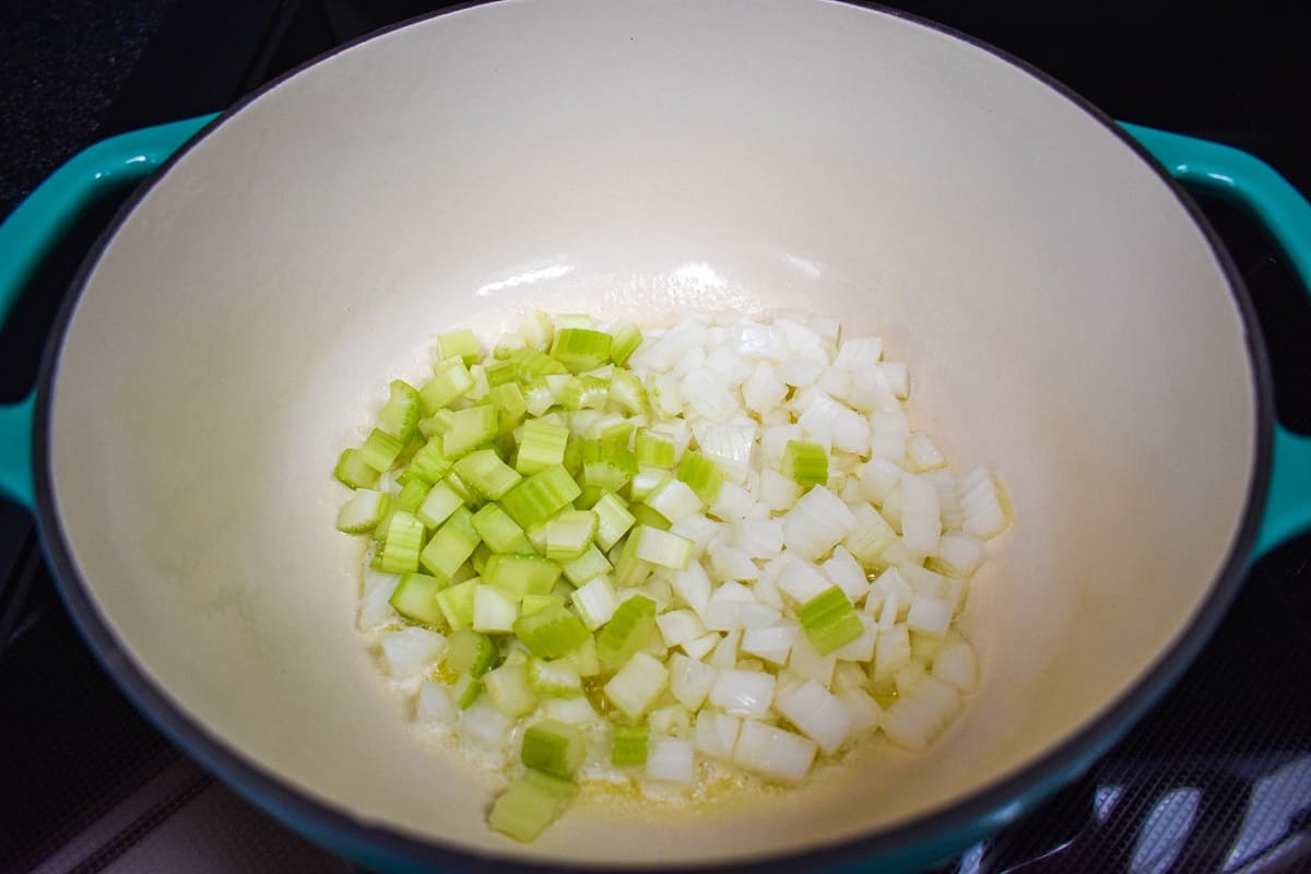 Diced onions and celery in a large, white and teal pot.