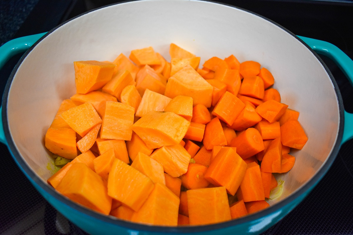 Cut carrots and sweet potatoes added to a large white and teal pot.