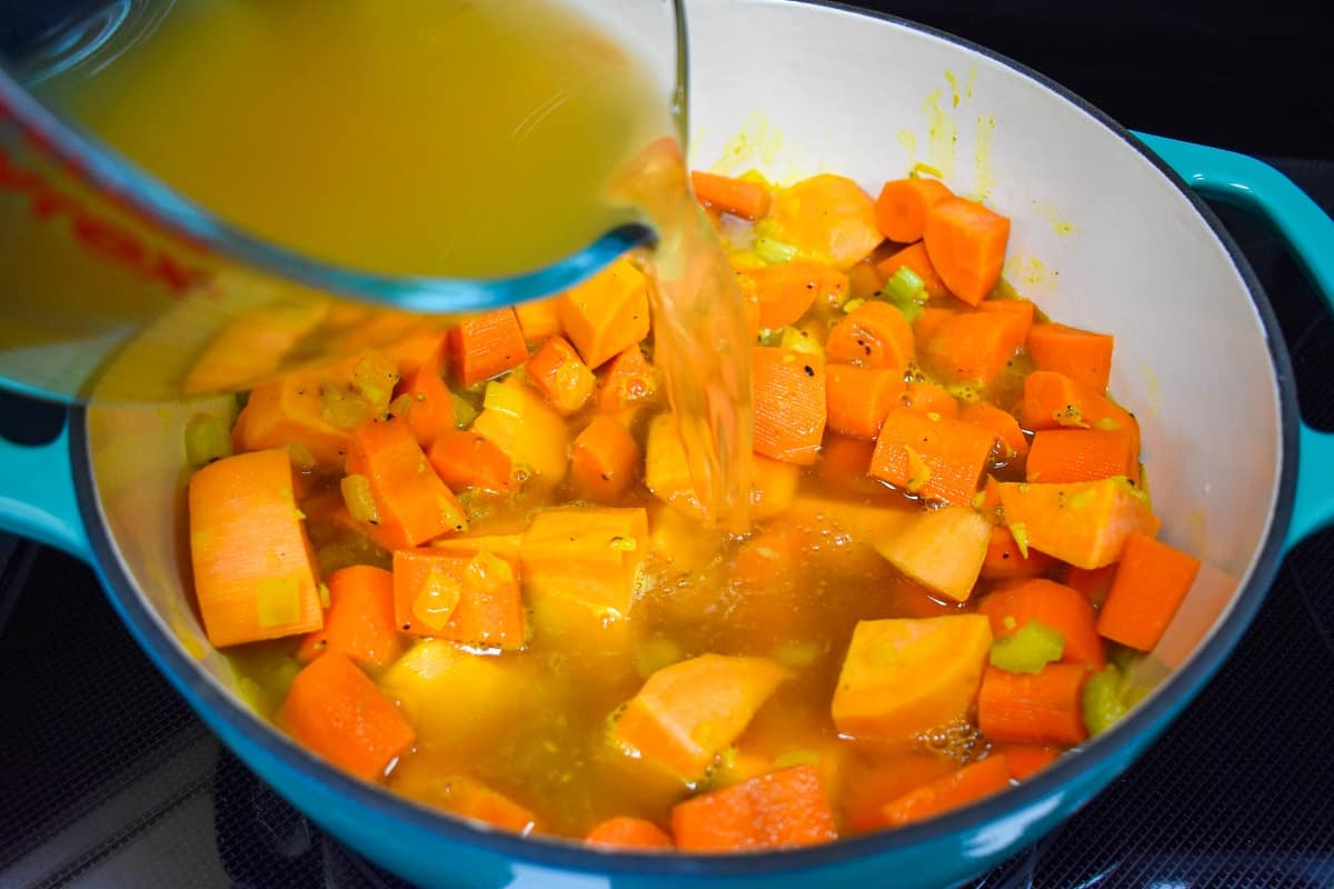 Chicken broth being added to the carrots, sweet potatoes and other ingredients in the pot.