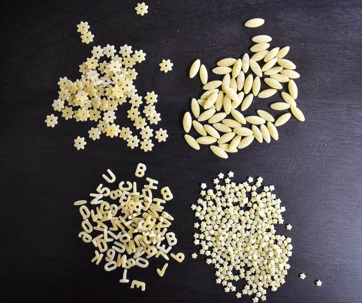 Four types of pastina arranged in little piles on a black cutting board.