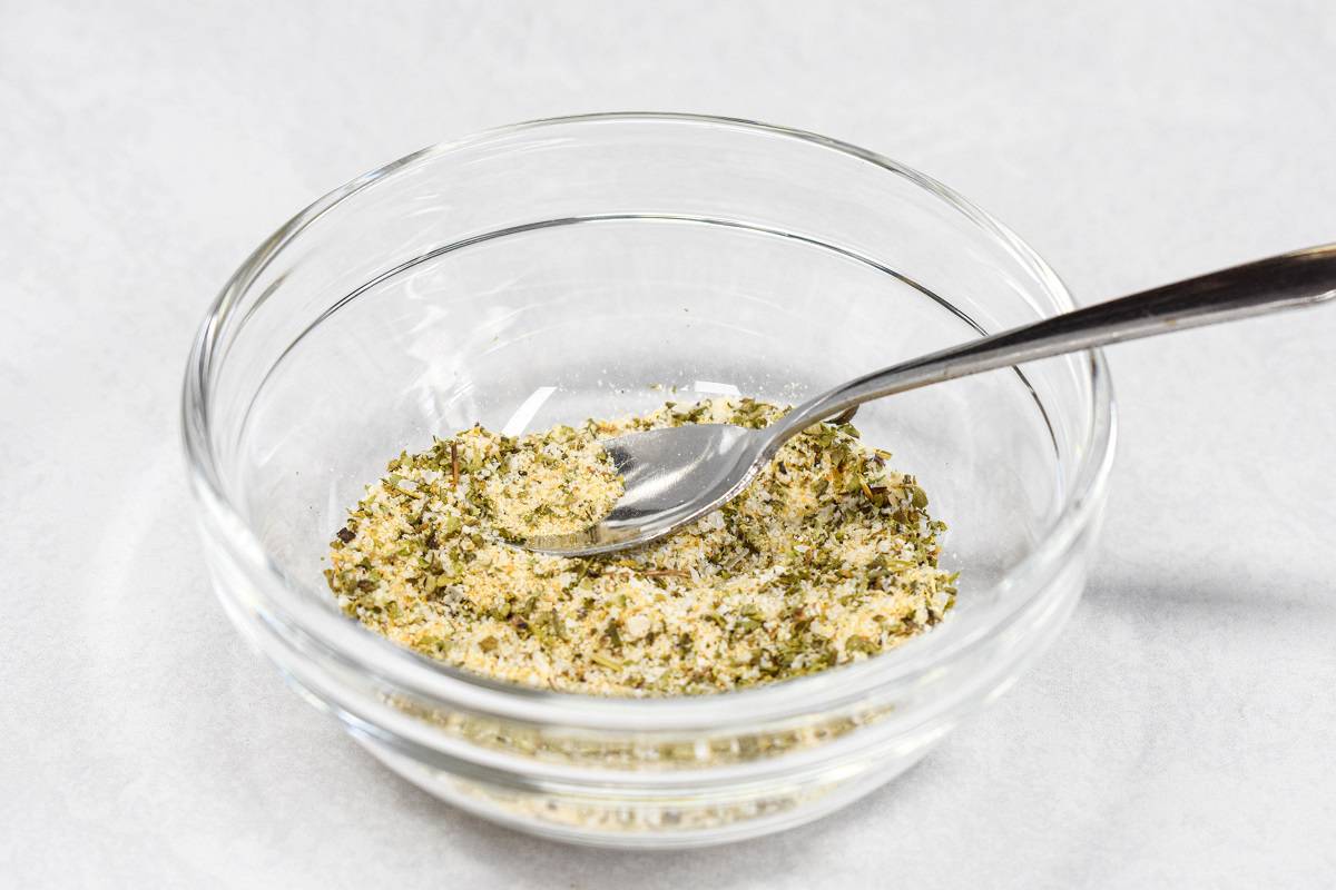 Salt, pepper, Italian seasoning, garlic and onion powder mixed in a small glass bowl with a small spoon.