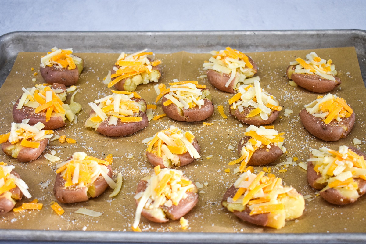 Shredded cheese topping all of the potatoes on the baking sheet.