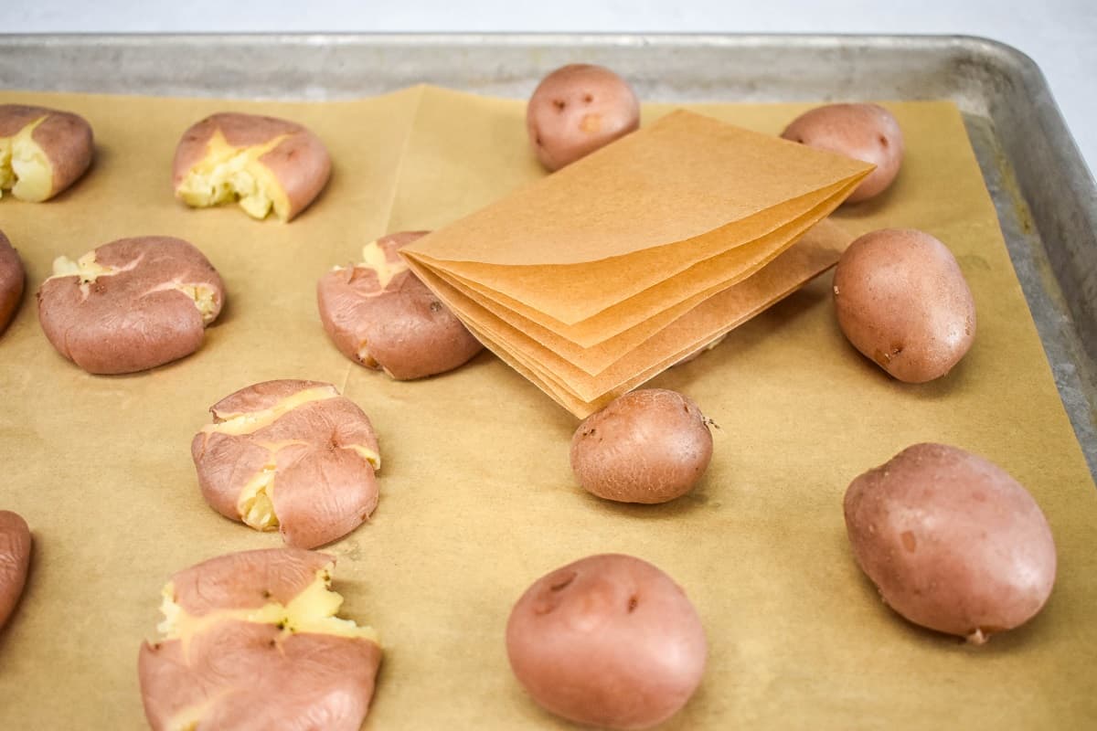 Red potatoes on a baking sheet lined with parchment paper with some smashed and some not and a folded piece of parchment paper.