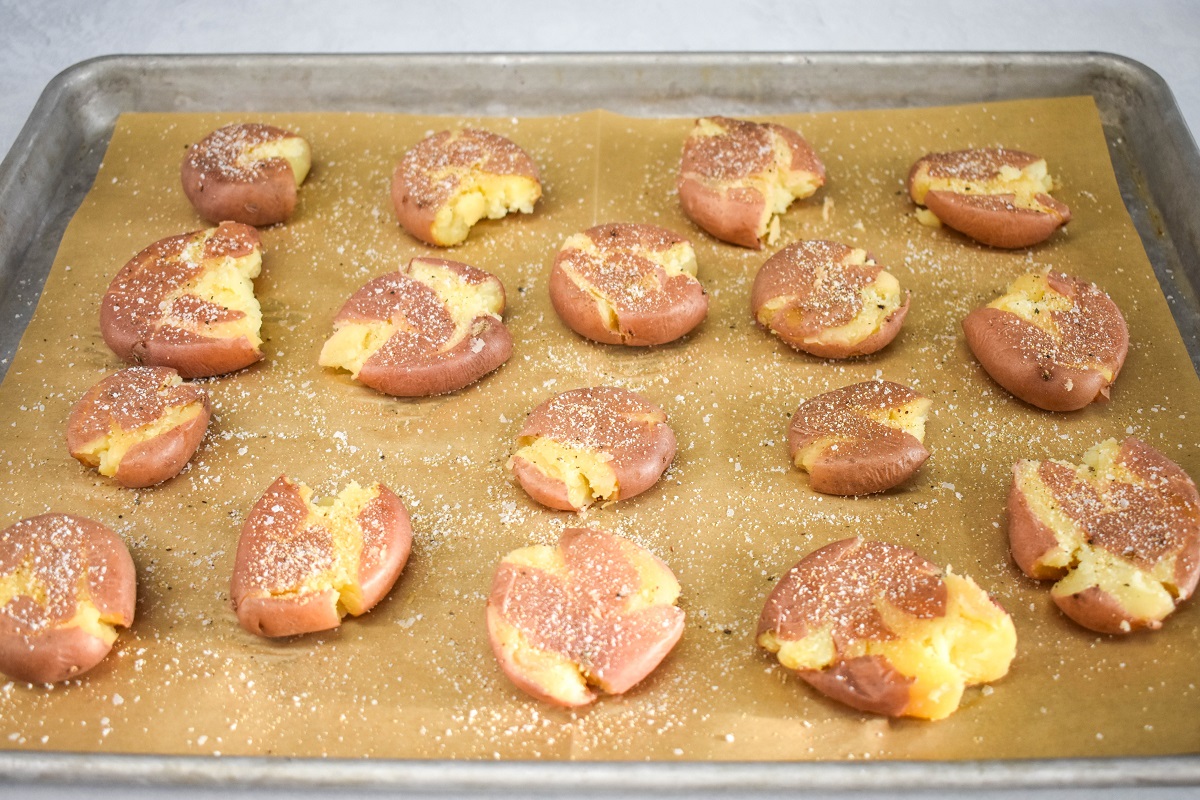 Seasoned smashed potatoes on a large baking sheet lined with parchment paper.