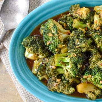 The stir-fried broccoli served in an aqua plate set on a beige table.