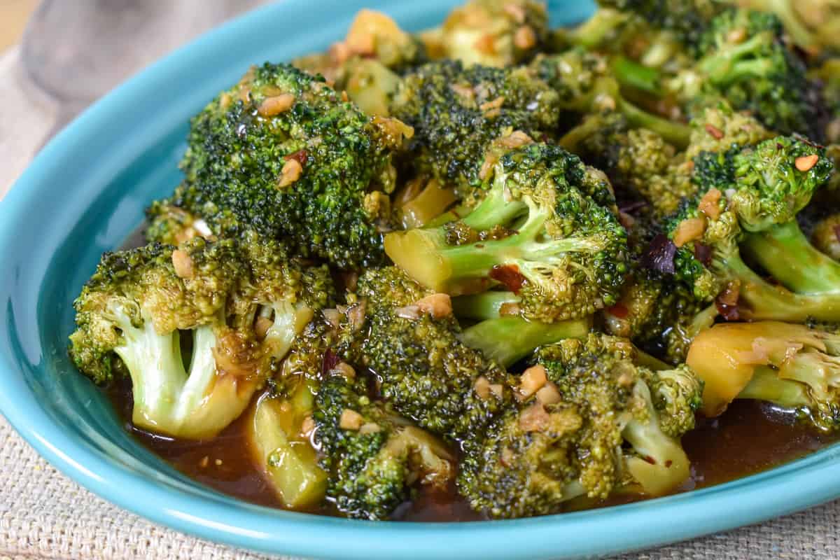 The stir-fried broccoli served in an aqua plate set on a beige table.