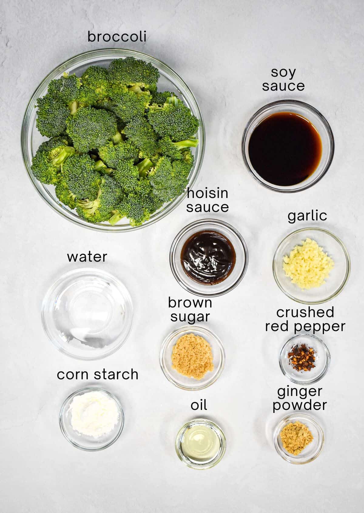 The ingredients for the dish prepped and arranged in glass bowls on a white table with each labeled with small, black letters.