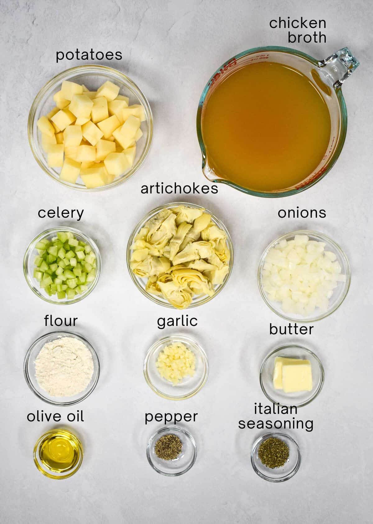 The ingredients for the soup prepped and arranged in glass bowls set on a white table with each labeled with small black letters.