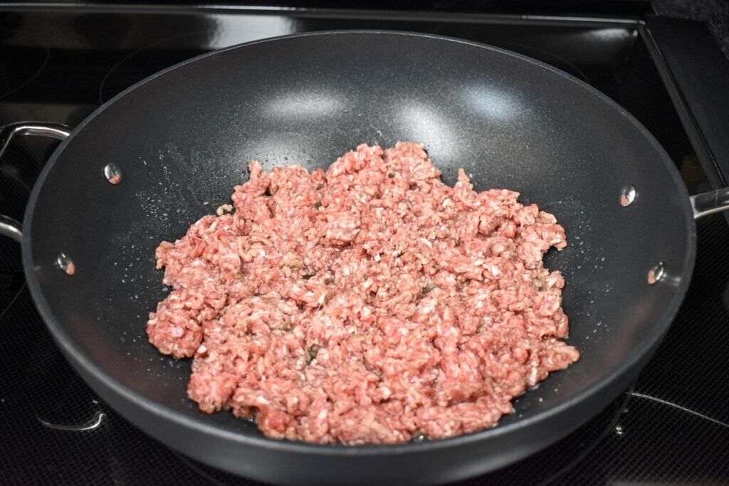 Raw ground beef arranged in a large, black skillet.