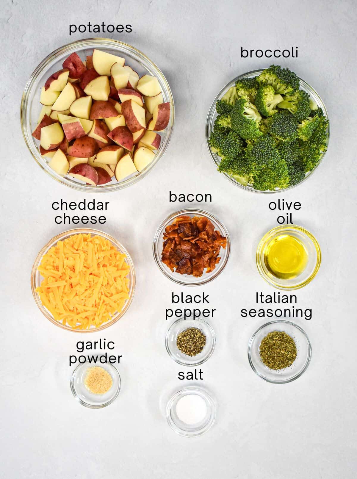 The ingredients for the dish prepped and arranged in glass bowls on a white table with each labled in small, black letters.