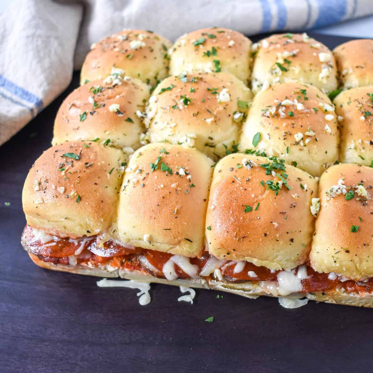 The sliders garnished with chopped parsley, set on a black board before they are cut apart.