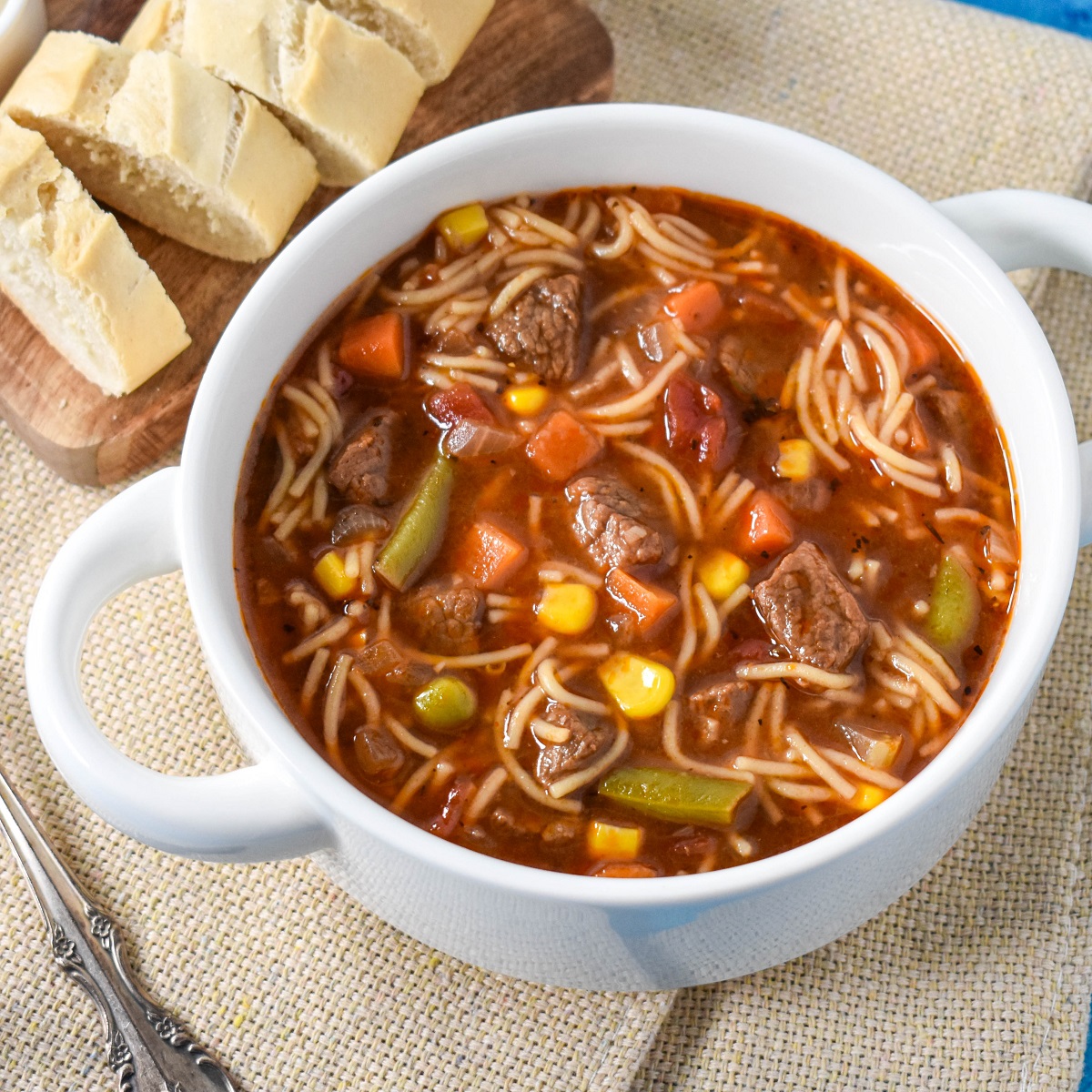 The beef noodle soup served in a white bowl with sliced bread and butter on a small cutting board in the back.