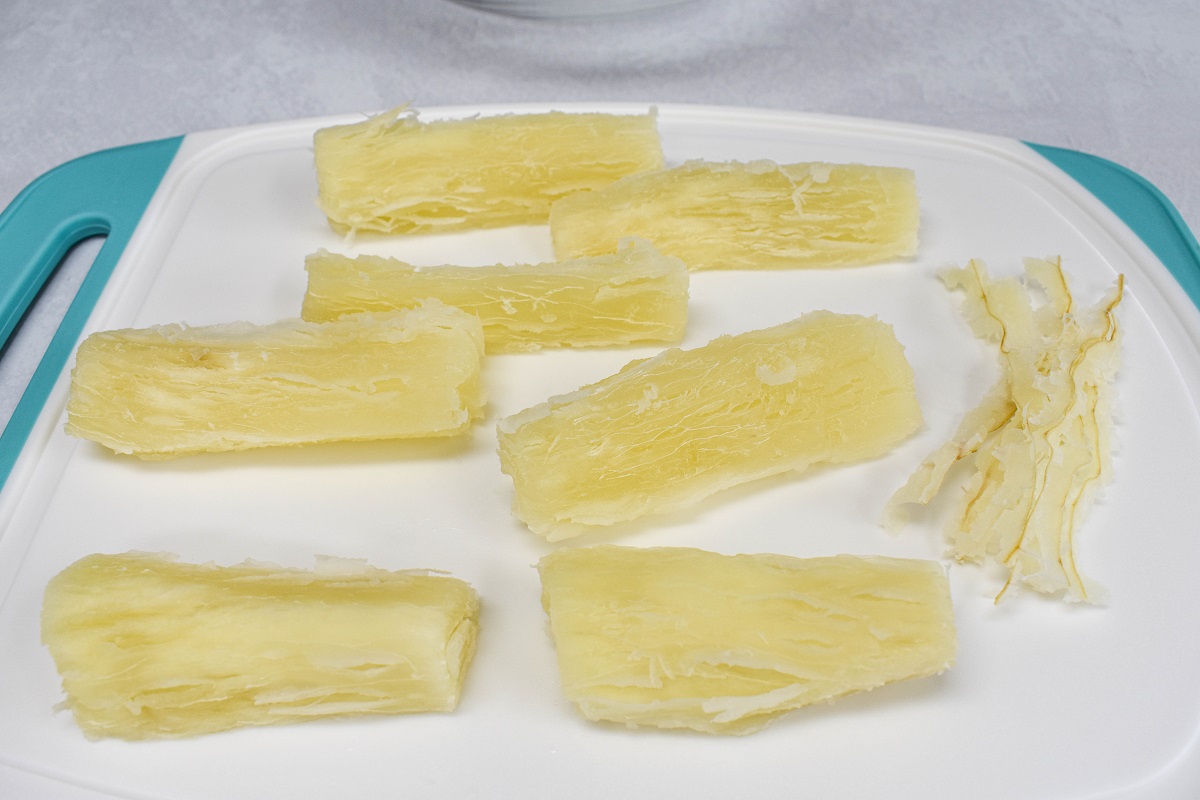 Cut pieces of yuca set on a white and teal cutting board with the woody stems removed and set to the right.