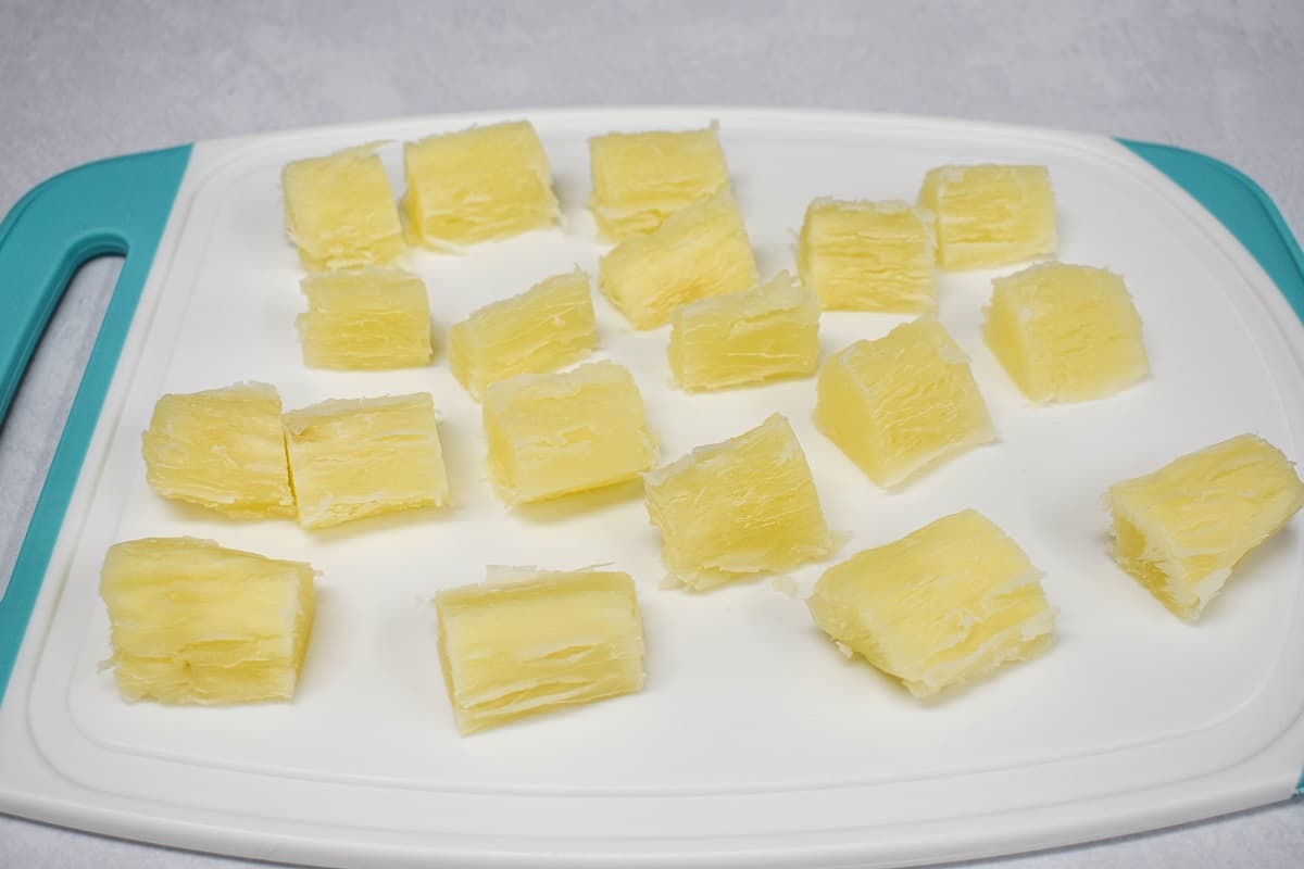 The cooked yuca cut into small pieces on a white and teal cutting board.