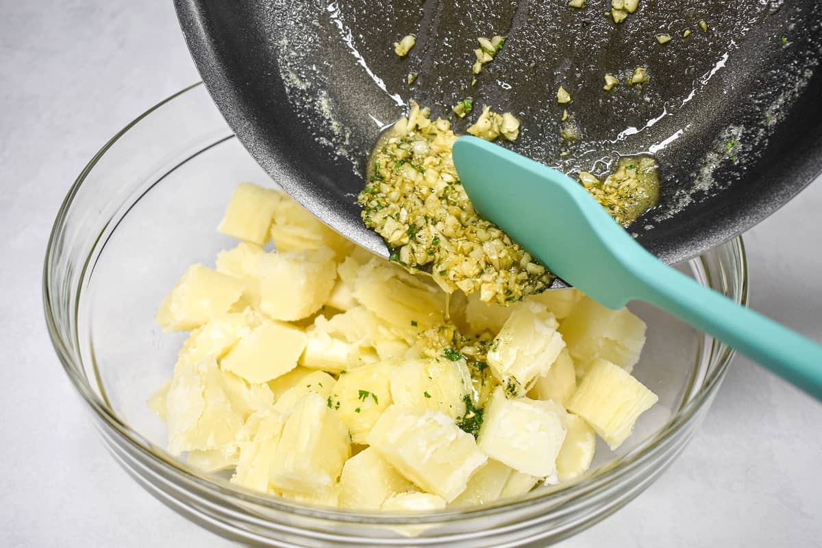 Garlic oil being added to the cut yuca in a large, glass bowl.