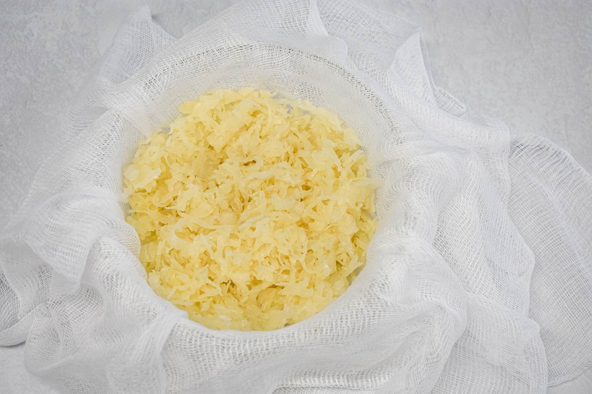 The sauerkraut in a bowl lined with cheese cloth set on a white table.