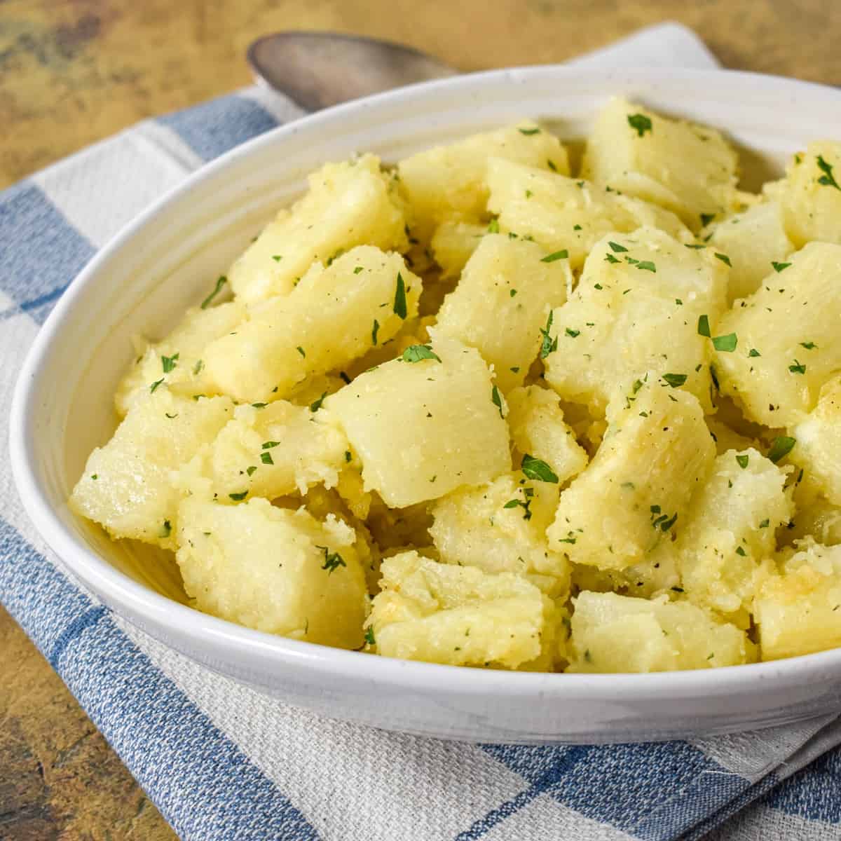 A close-up of the yuca with garlic sauce served in an oval white bowl set on a blue and white linen.