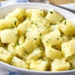 The yuca with garlic sauce served in an oval white bowl set on a blue and white linen with a serving spoon and a graphic with the title in white letters.