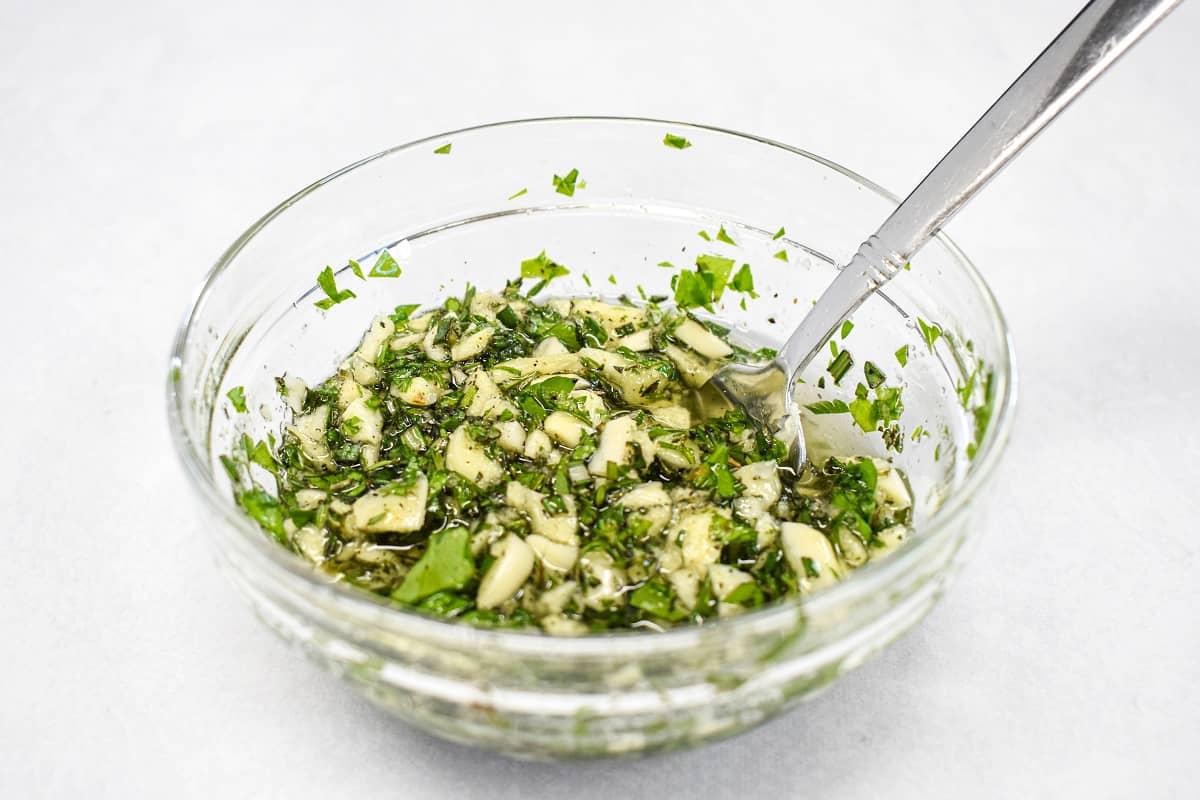 The garlic and herb rub combined in a small bowl set on a white table.