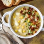 The potato corn chowder garnished with bacon bits and chives served in a white bowl.