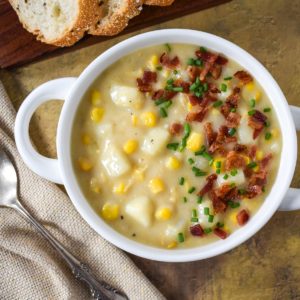The potato corn chowder garnished with bacon bits and chives served in a white bowl.