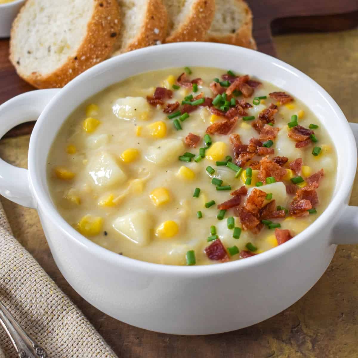 A close up of the finished soup served in a white bowl with sliced bread in the background.