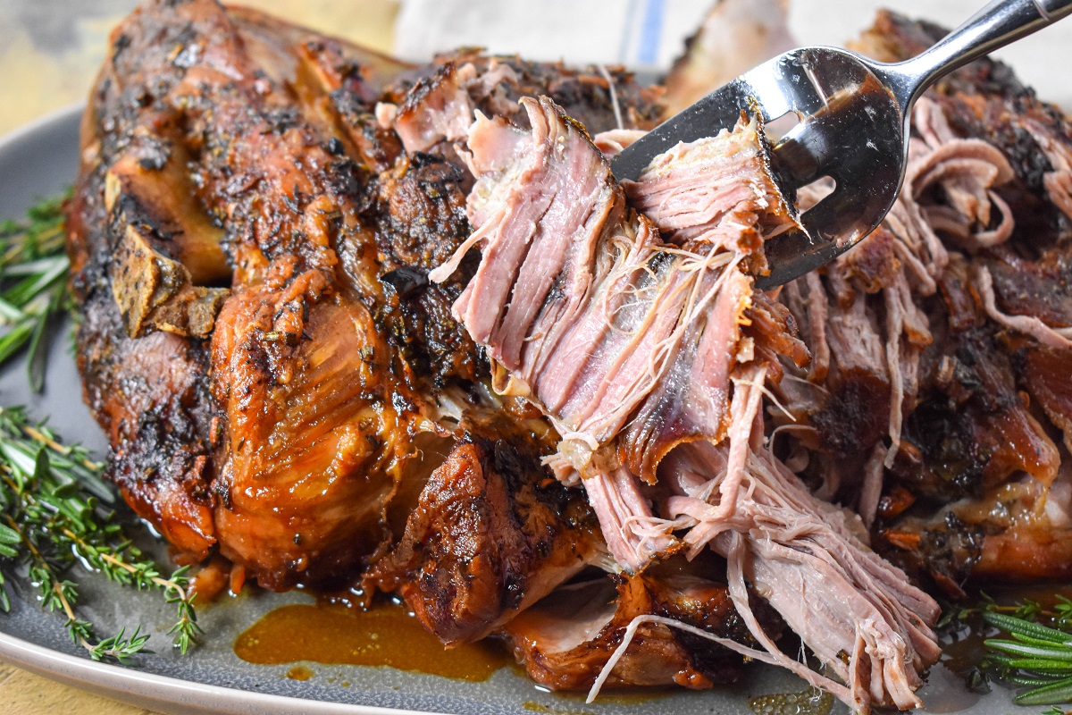 The pork butt on a large, gray platter with a piece being held up with a large serving fork.