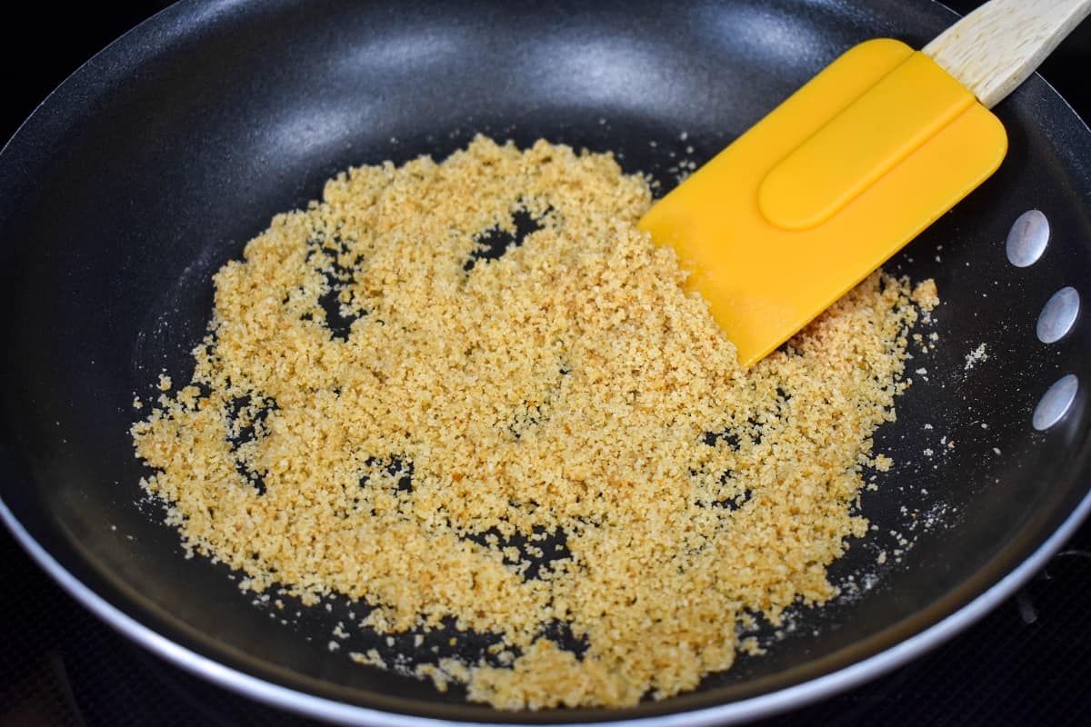 Butter and breadcrumbs combined in a non-stick skillet with an orange spatula to the right side.