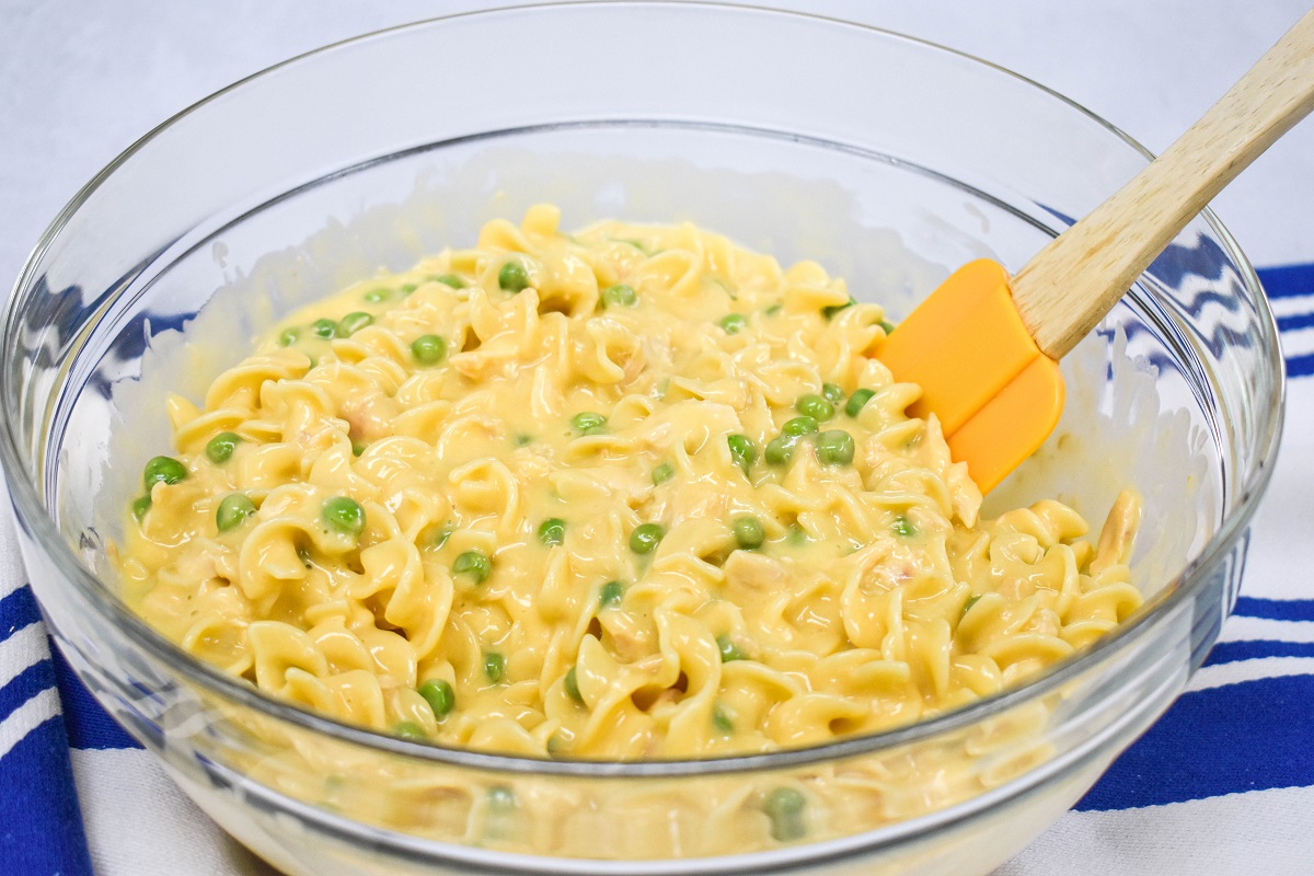 The ingredients for the casserole combined in a large, glass bowl with an orange spatula to the right side.