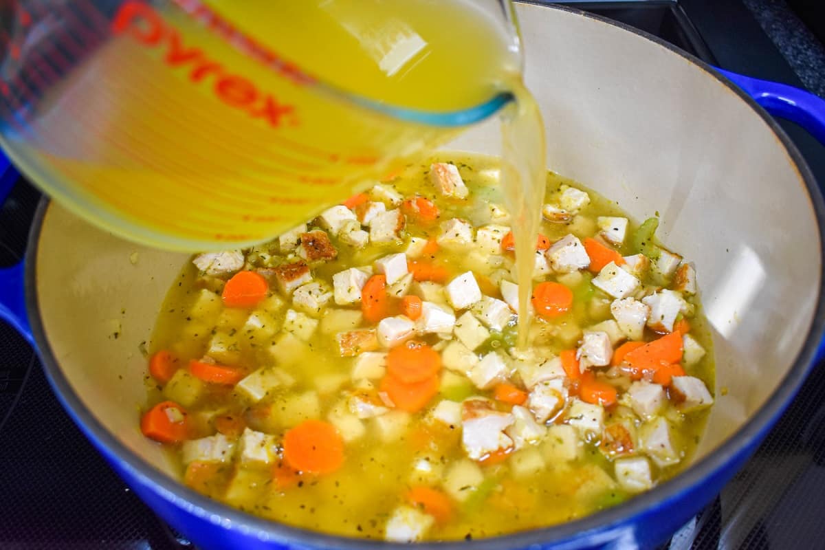 Chicken broth being added to the diced turkey and vegetables in a large pot.