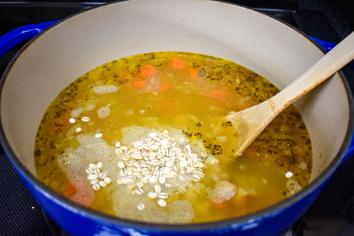 Barley added to the soup in the pot with a wooden spoon to the right side.