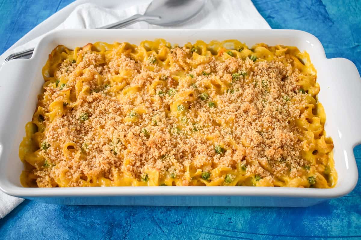 The baked tuna noodle casserole in a white casserole dish set on a blue table with a white linen.