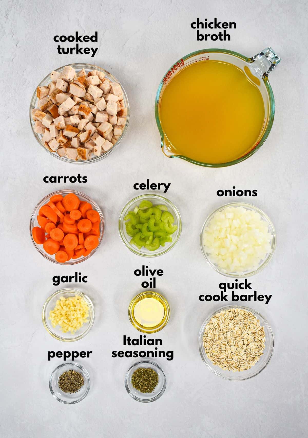 The ingredients for the soup prepped and arranged in glass bowls set on a white table with each one labeled with small, black letters.