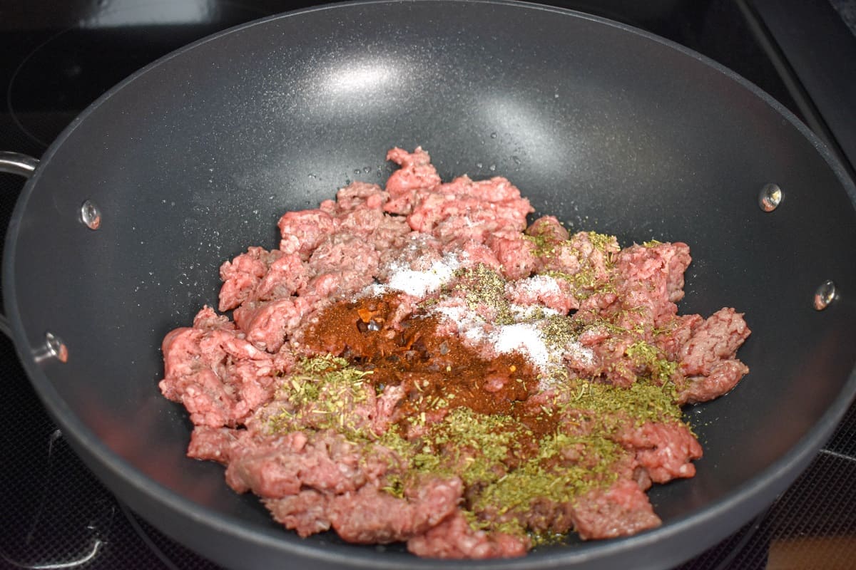Ground beef with spices in a large, non-stick skillet before mixing and browning.