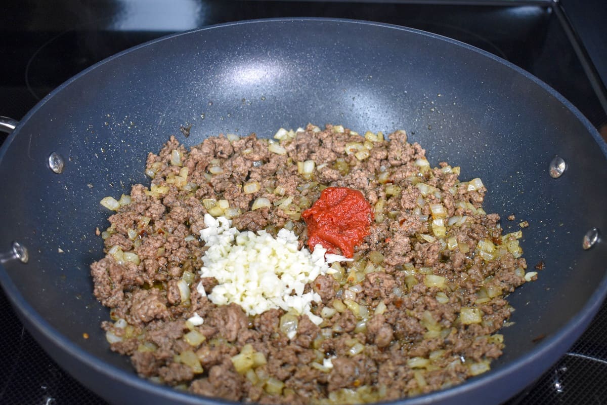 Minced garlic and tomato paste added to browned ground beef in a skillet.
