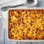 The macaroni and beef casserole in a white baking dish with a serving spoon and white linen in the background.