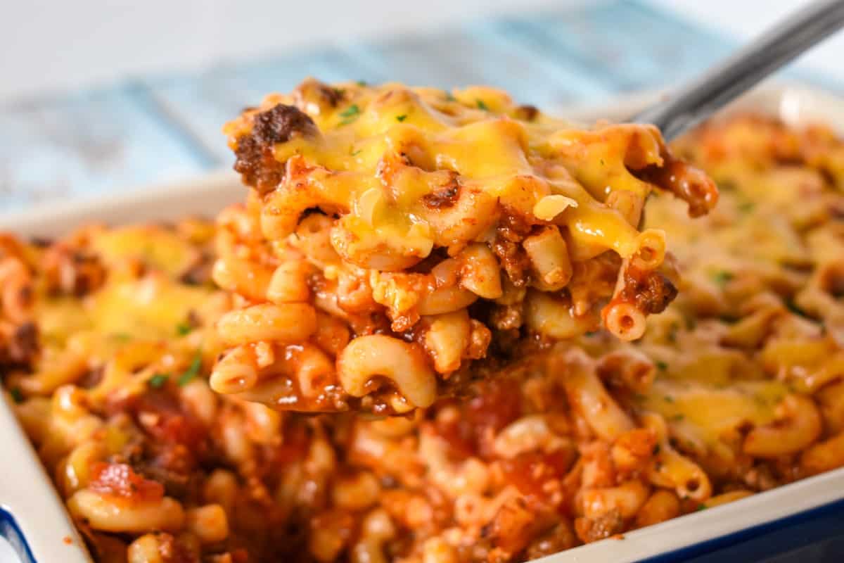 A serving of the pasta casserole lifted over the baking dish with a large serving spoon.