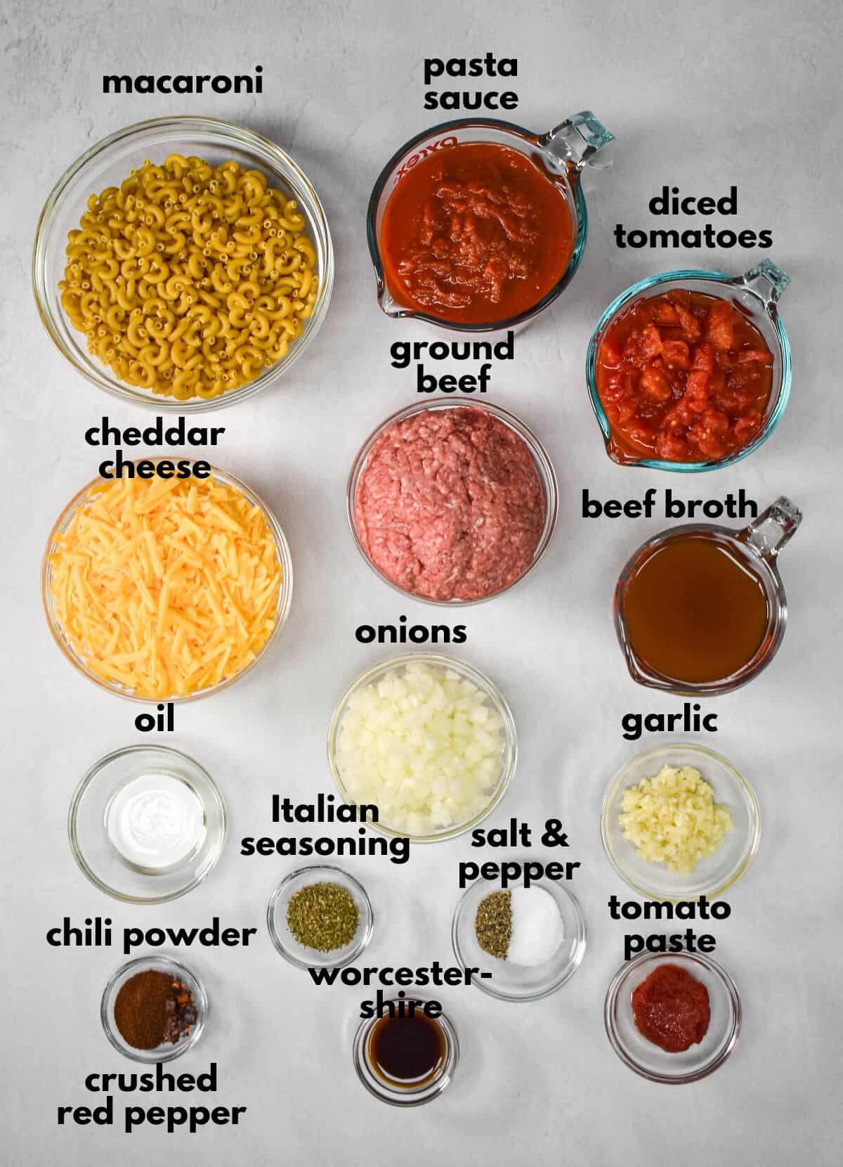 The ingredients for the pasta casserole prepped and arranged in glass bowls on a table with each labeled with small, black letters.