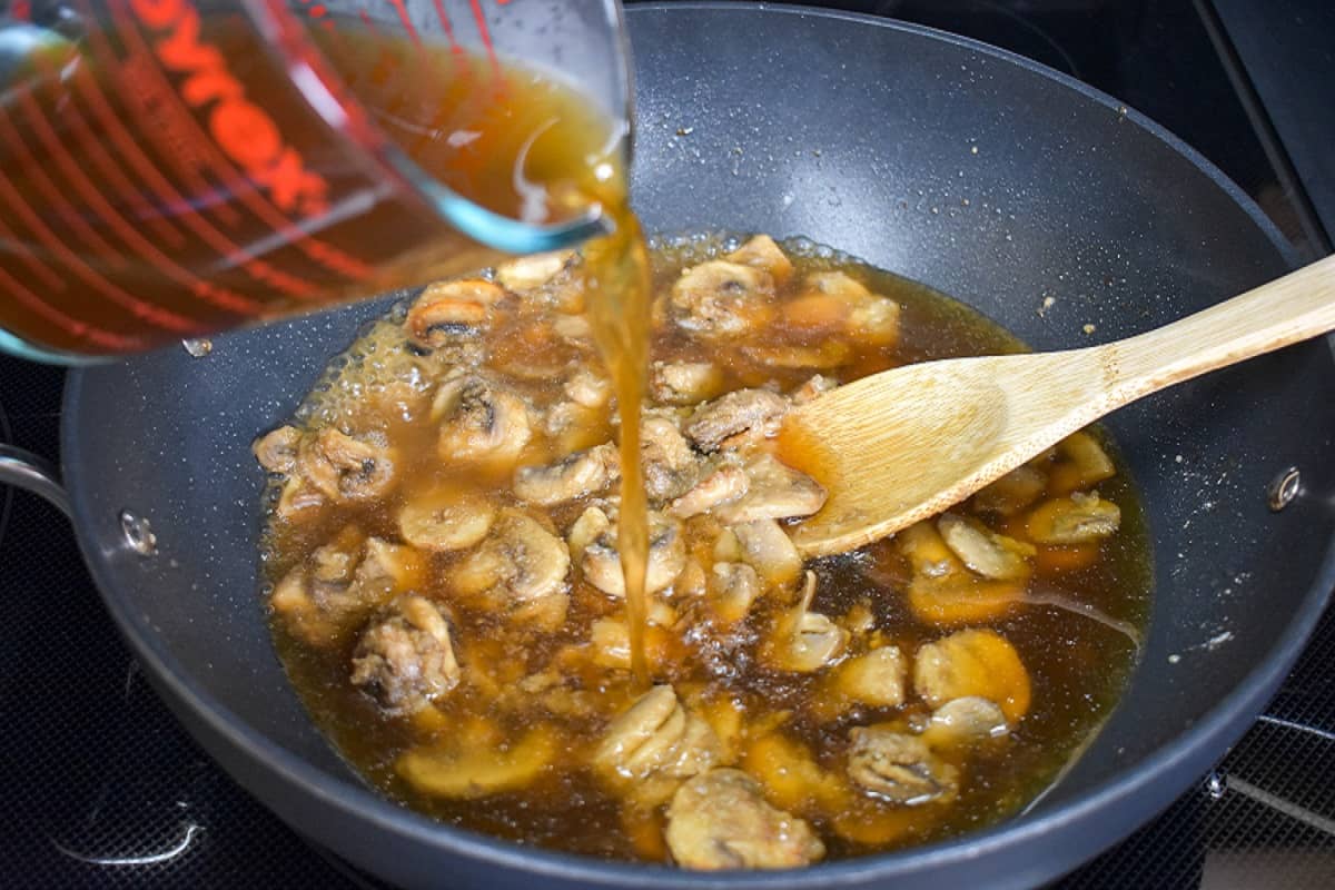 Beef broth being added to the mushroom mixture in the skillet.