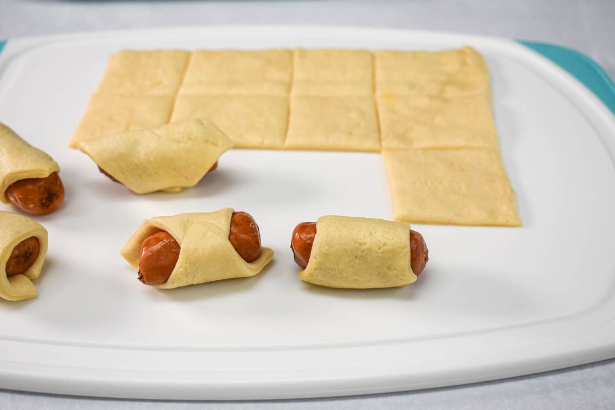 A few cocktail sausage wrapped in dough on a cutting board.