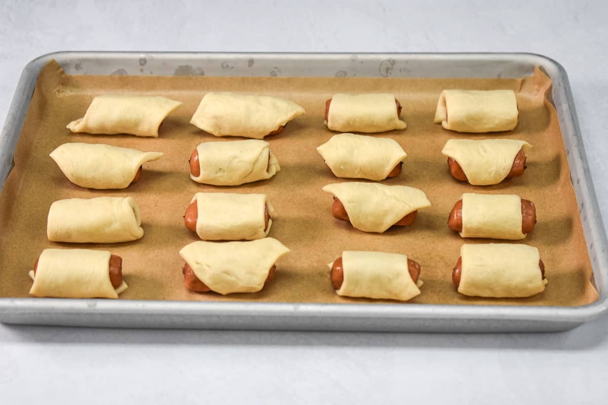 The rolled sausages arranged in rows on a baking sheet lined with parchment paper.