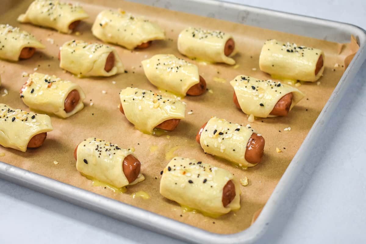 The prepared pigs in a blanket arranged on a baking sheet before baking.