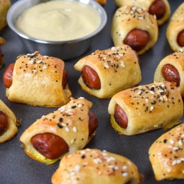 Pigs in a blanket set on a gray platter with a small bowl of mustard.