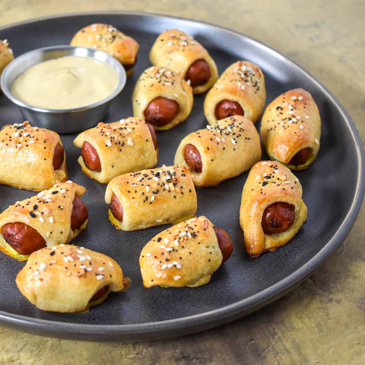 The pigs in a blanket arranged on a gray platter served with a side of mustard.