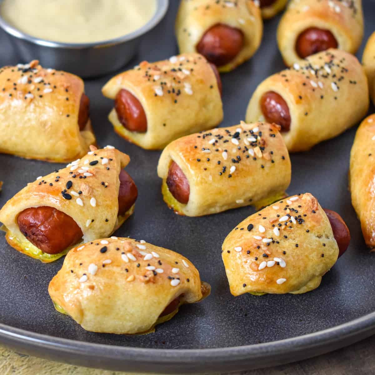 The pigs in a blanket arranged on a gray platter served with a side of mustard.