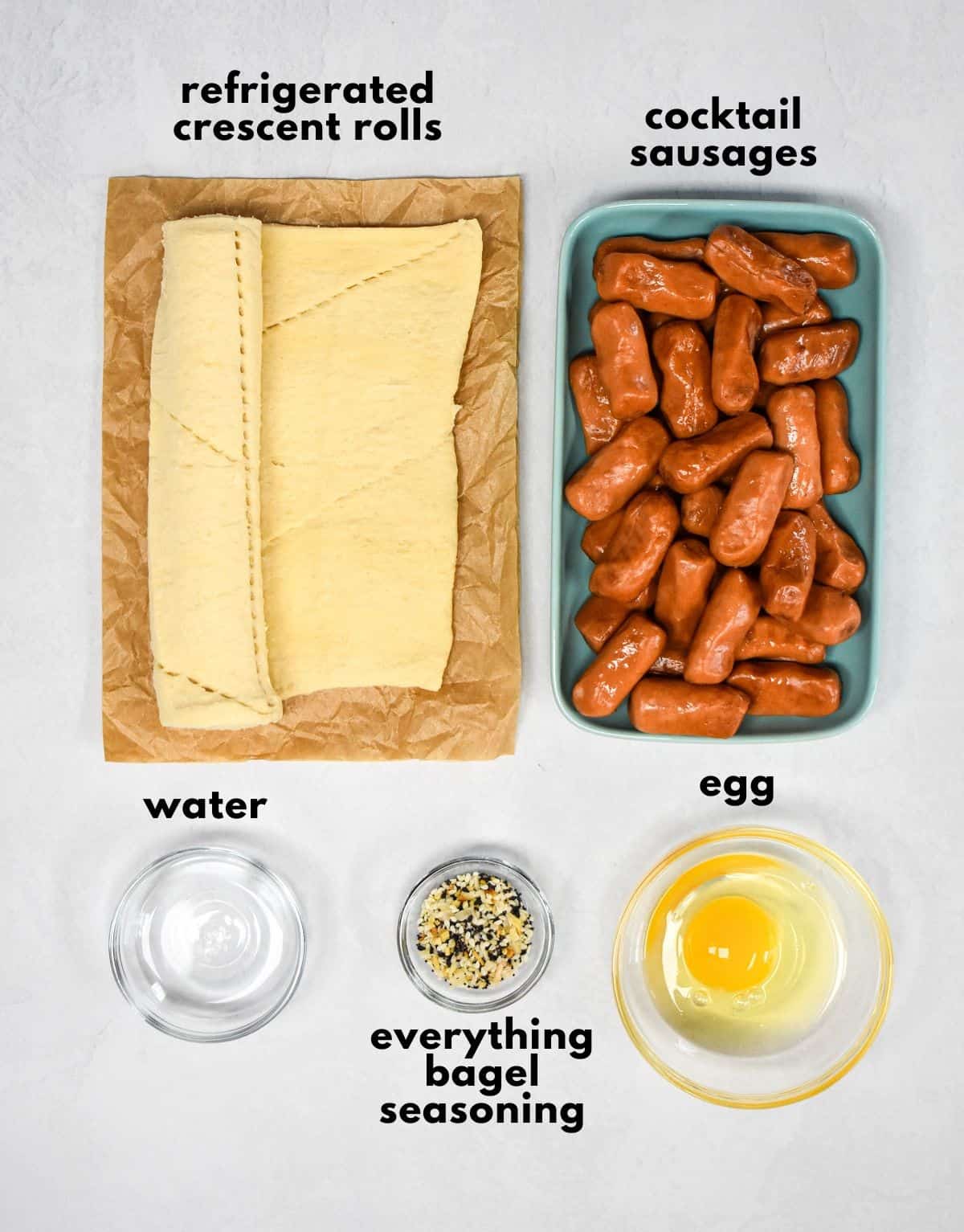 The ingredients for the pigs in a blanket arranged on a table with each labeled in small black letters.