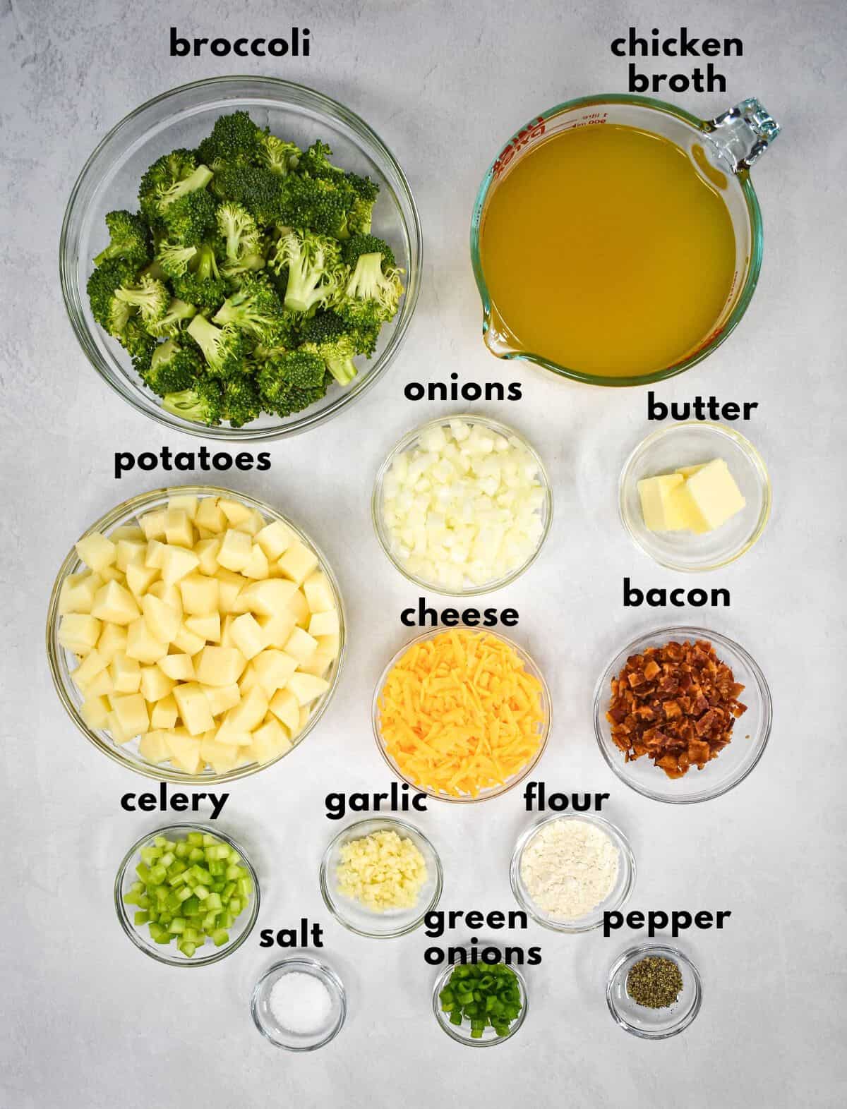 The ingredients for the soup prepped and arranged in glass bowls on a white table with each ingredient labeled with small, black letters.