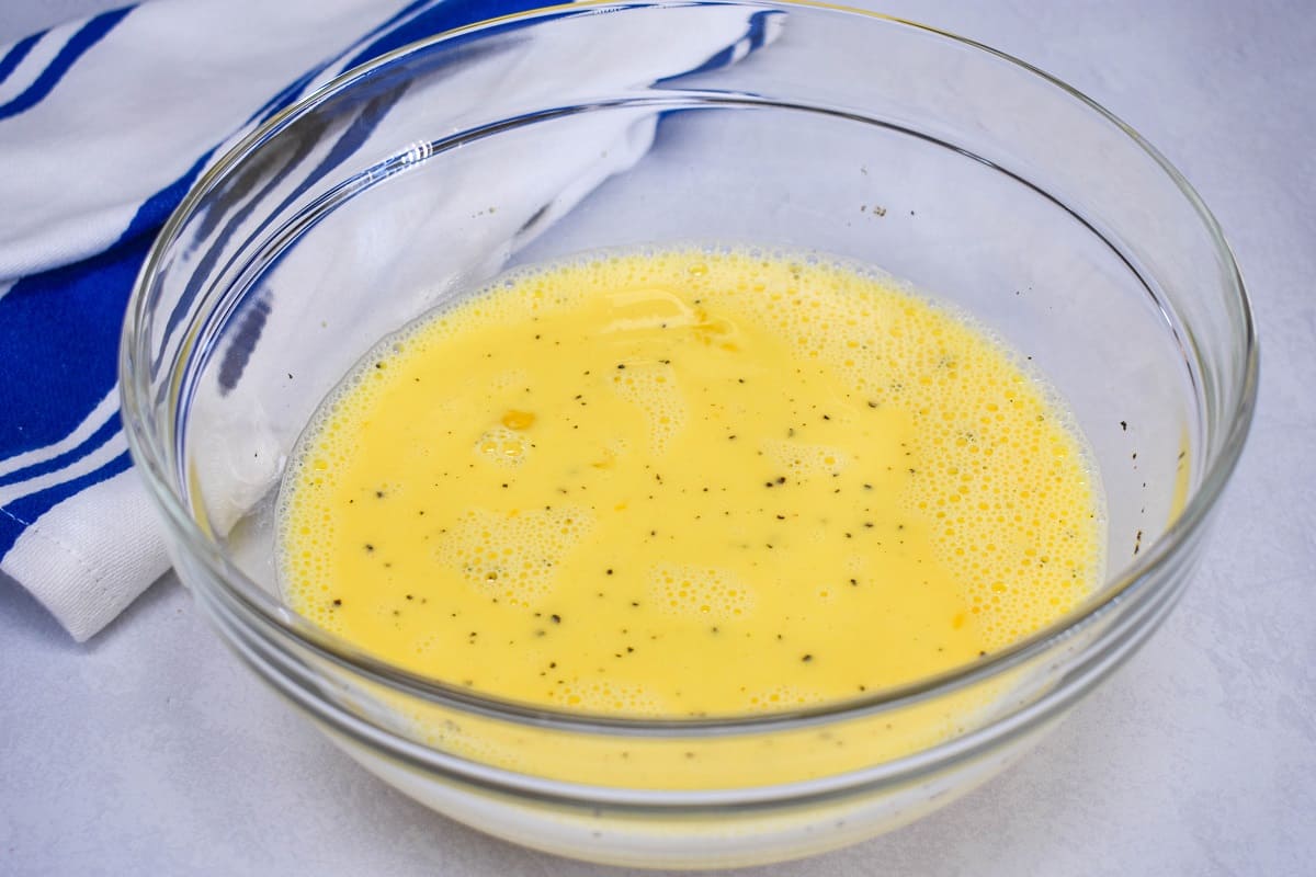Eggs and milk whisked together in a large, glass bowl.