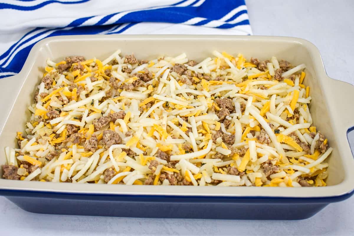 The sausage, hash brown, cheese mixture arranged in a blue casserole dish.