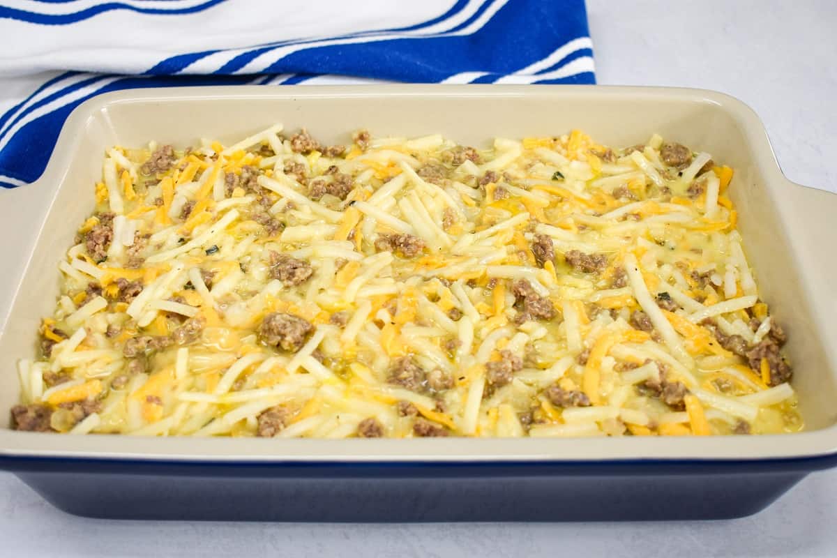 The prepared breakfast casserole before adding the cheese topping in a blue baking dish.